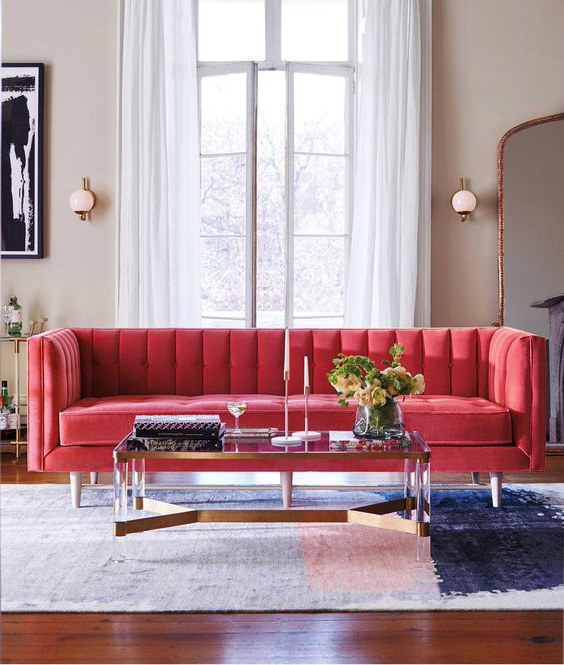 Divano rosso fragola su soggirono moderno con tappeto in toni del grigio e rosa.